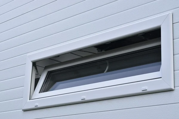 Weißes Kippfenster in einer Sandwichpaneelwand eines Carports