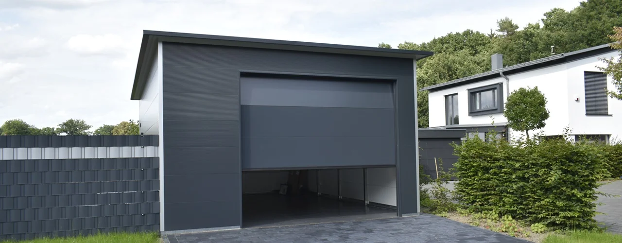 Moderner Garagenbau aus Sandwichpaneelen mit geöffnetem, glattem Sektionaltor in Anthrazit – großzügige Einfahrt und hochwertige Verarbeitung im Detail