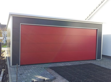 Moderne Doppel-Fertiggarage mit rotem Sektionaltor und Sandwichpaneelen, isoliert und nach Maß gebaut