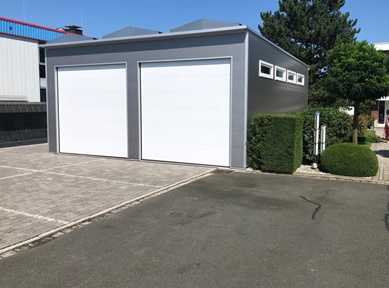 Moderne Doppel-Fertiggarage mit zwei weißen Sektionaltoren und Sandwichpaneelen, isoliert und nach Maß gebaut