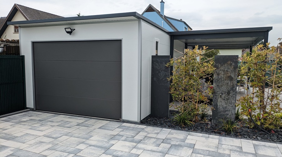 Moderne Fertiggarage aus Sandwichpaneelen mit anthrazitfarbenem Sektionaltor und Flachdach – hochwertige und isolierte Garagenlösung. Isolierte Garage mit Sandwichpaneel-Fassade, glattem Sektionaltor in Anthrazit und angrenzendem Carport. Hochwertige Fertiggarage mit Wärmedämmung, Sandwichpaneel-Wänden und modernem Flachdachdesign. Sandwichpaneel-Garage mit pflegeleichter Fassade, isoliertem Sektionaltor und eleganter Hofeinfahrt. Freistehende Garage mit Sandwichpaneel-Konstruktion und Sektionaltor in zeitlosem Anthrazitgrau