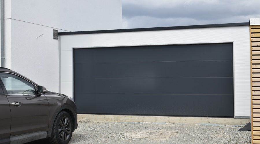Einzelgarage aus Sandwichpaneelen mit glattem, anthrazitfarbenem Sektionaltor und modernem Flachdach. Moderne Fertiggarage mit isoliertem Sektionaltor in Anthrazit und weißer Sandwichpaneel-Fassade. Isolierte Einzelgarage mit pflegeleichter Sandwichpaneel-Konstruktion und zeitlosem Design. Hochwertige Einzelgarage aus Sandwichpaneelen mit Wärmedämmung und modernem Sektionaltor. Freistehende Einzelgarage mit anthrazitfarbenem Sektionaltor und weißer Fassade aus Sandwichpaneelen