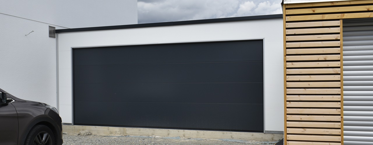 Breite moderne Anbaugarage mit anthrazitfarbenem Sektionaltor und weißer Fassade