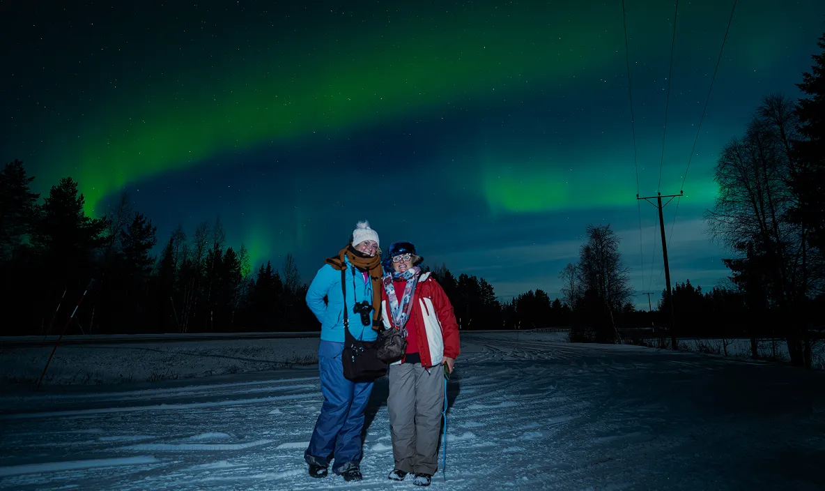 Two tourists on snowy road with aurora.