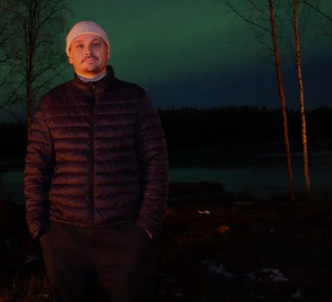 Man in winterwear under aurora sky.