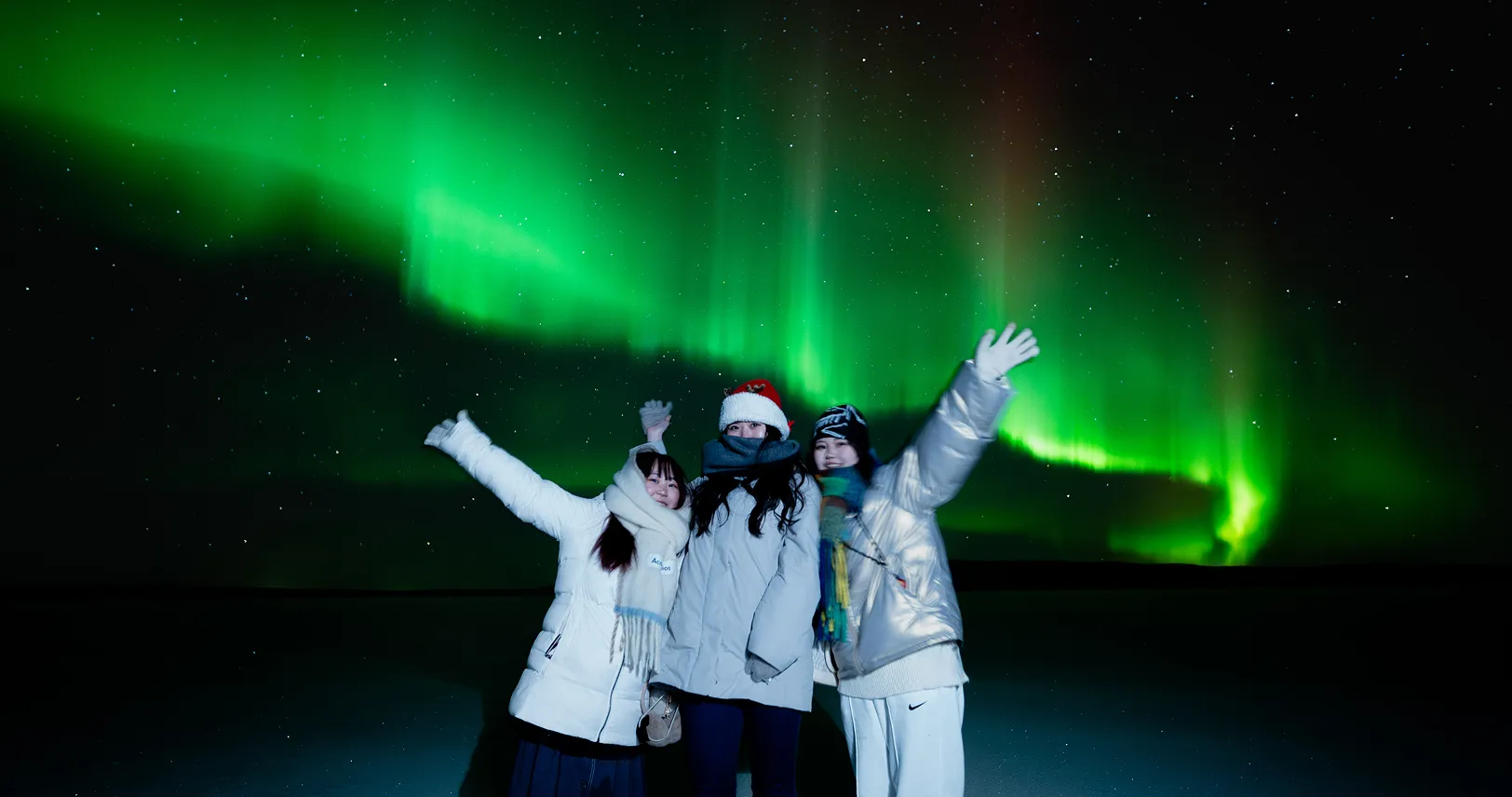 Three friends under bright aurora display.