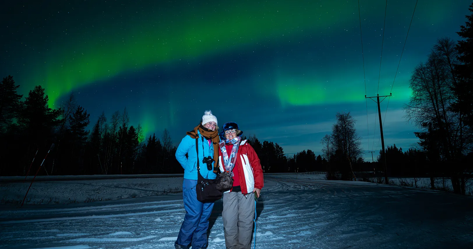 Two tourists on snowy road with aurora.