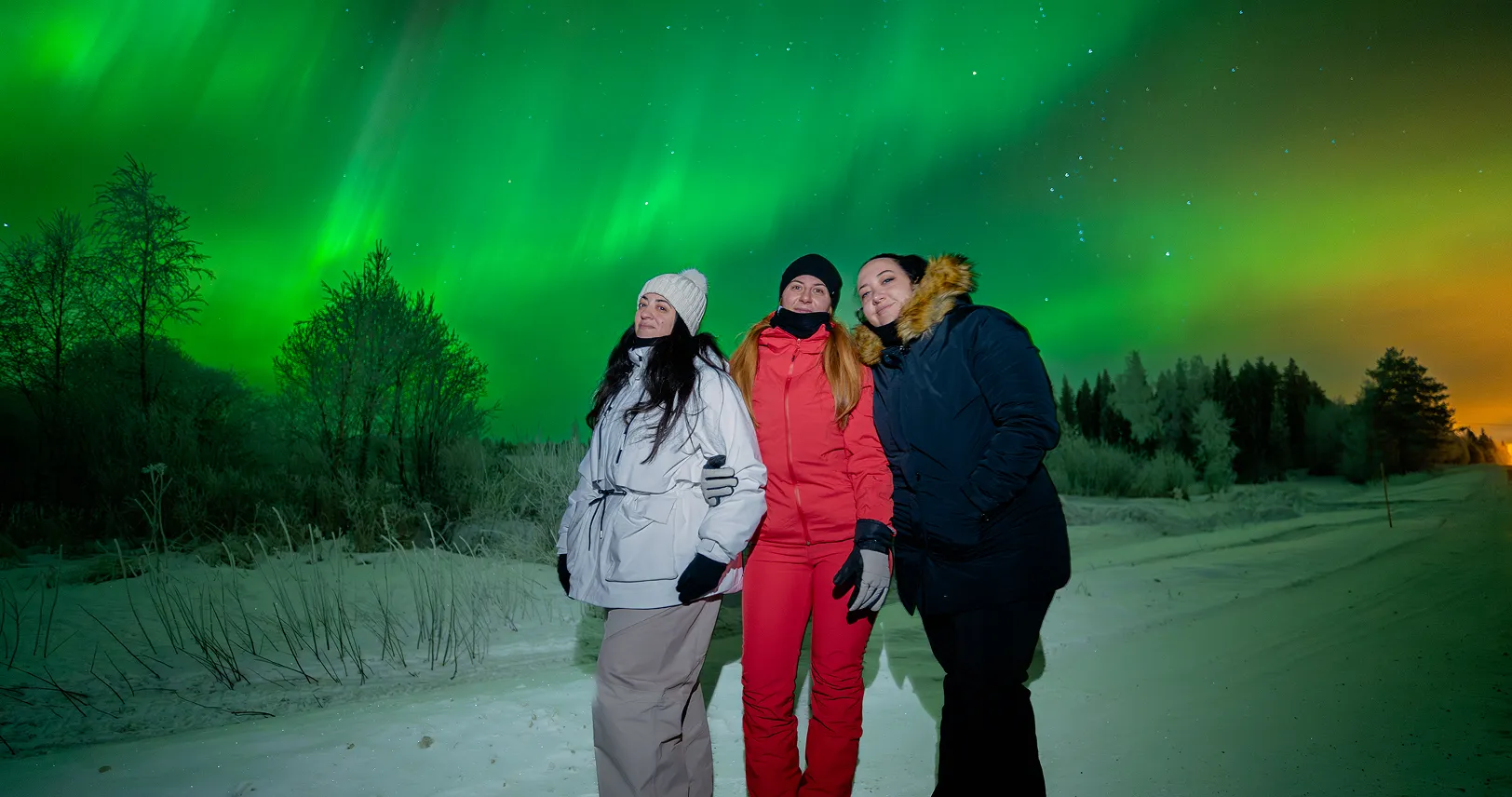 Three women posing under green aurora.