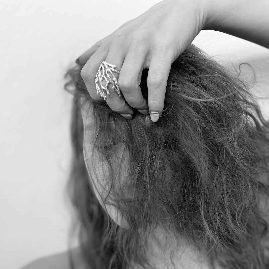 black and white image of a woman with messy hair and her hand with a carved silver ring