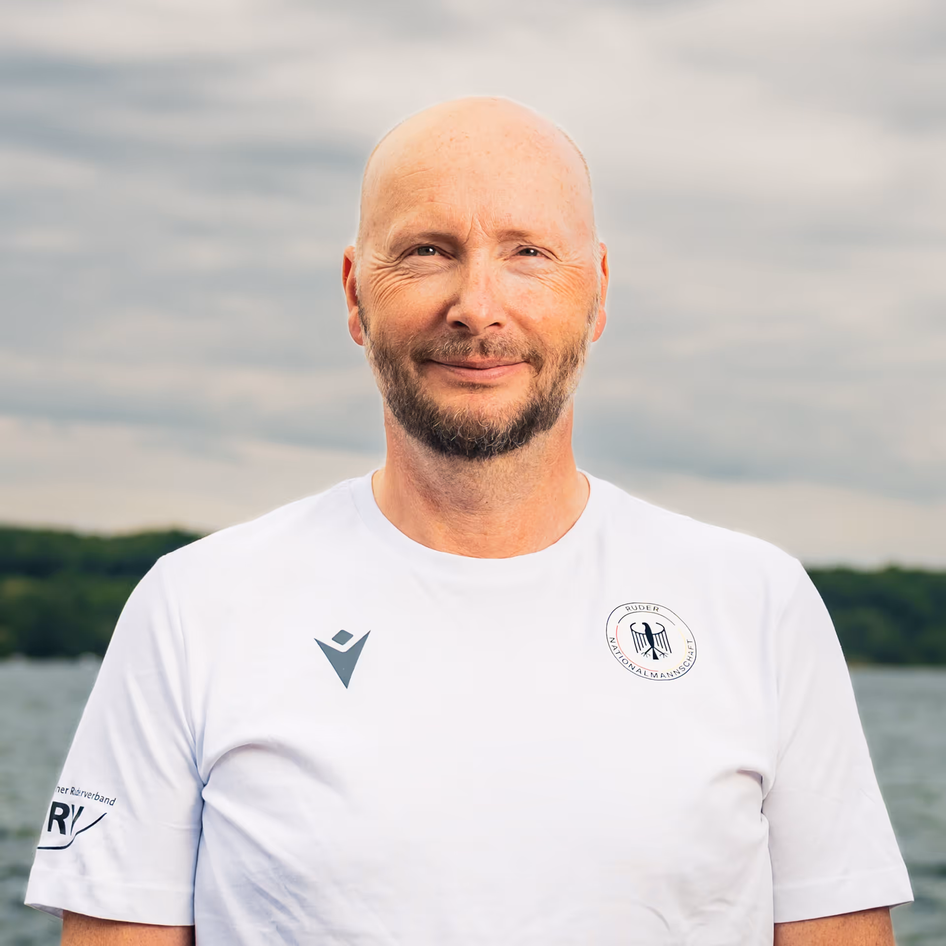 Porträt von Alexander Schmidt, Trainer im deutschen Nationalteam, vor wolkigem Himmel am Wasser.
