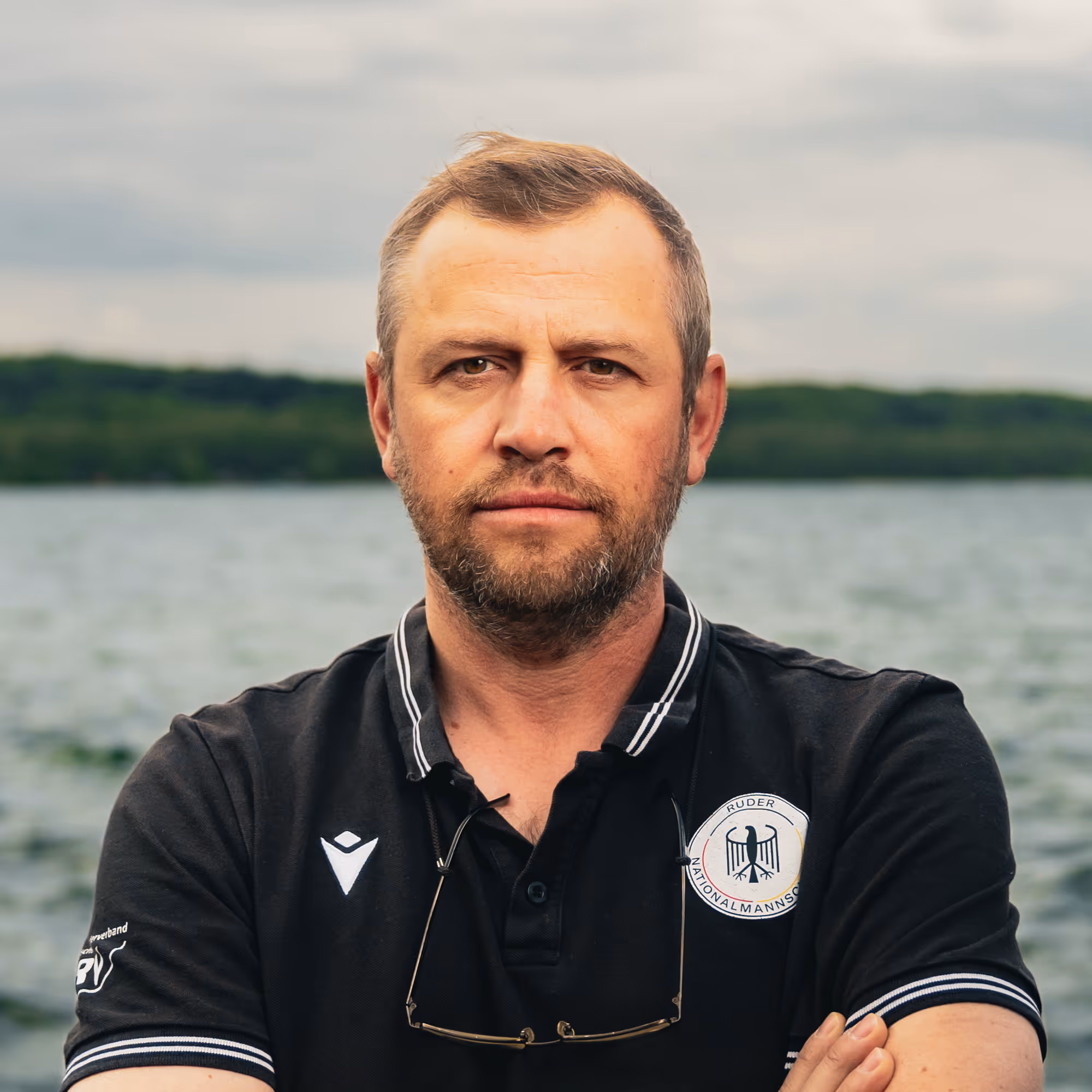 Porträt von Marcin Witkowski, Trainer im deutschen Nationalteam, vor wolkigem Himmel am Wasser.