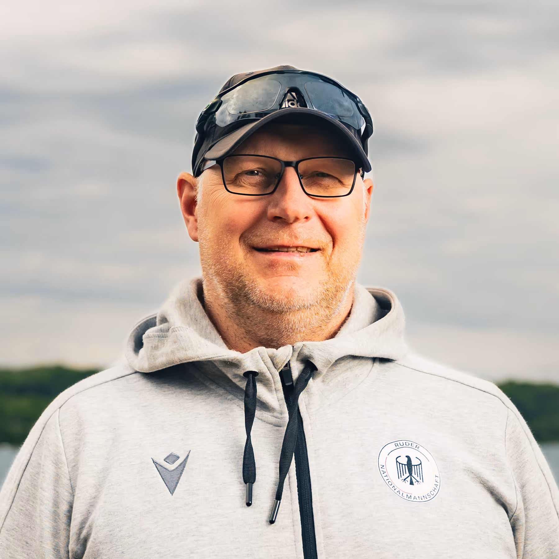 Porträt von Sven Ueck, Trainer im deutschen Nationalteam, vor wolkigem Himmel am Wasser.