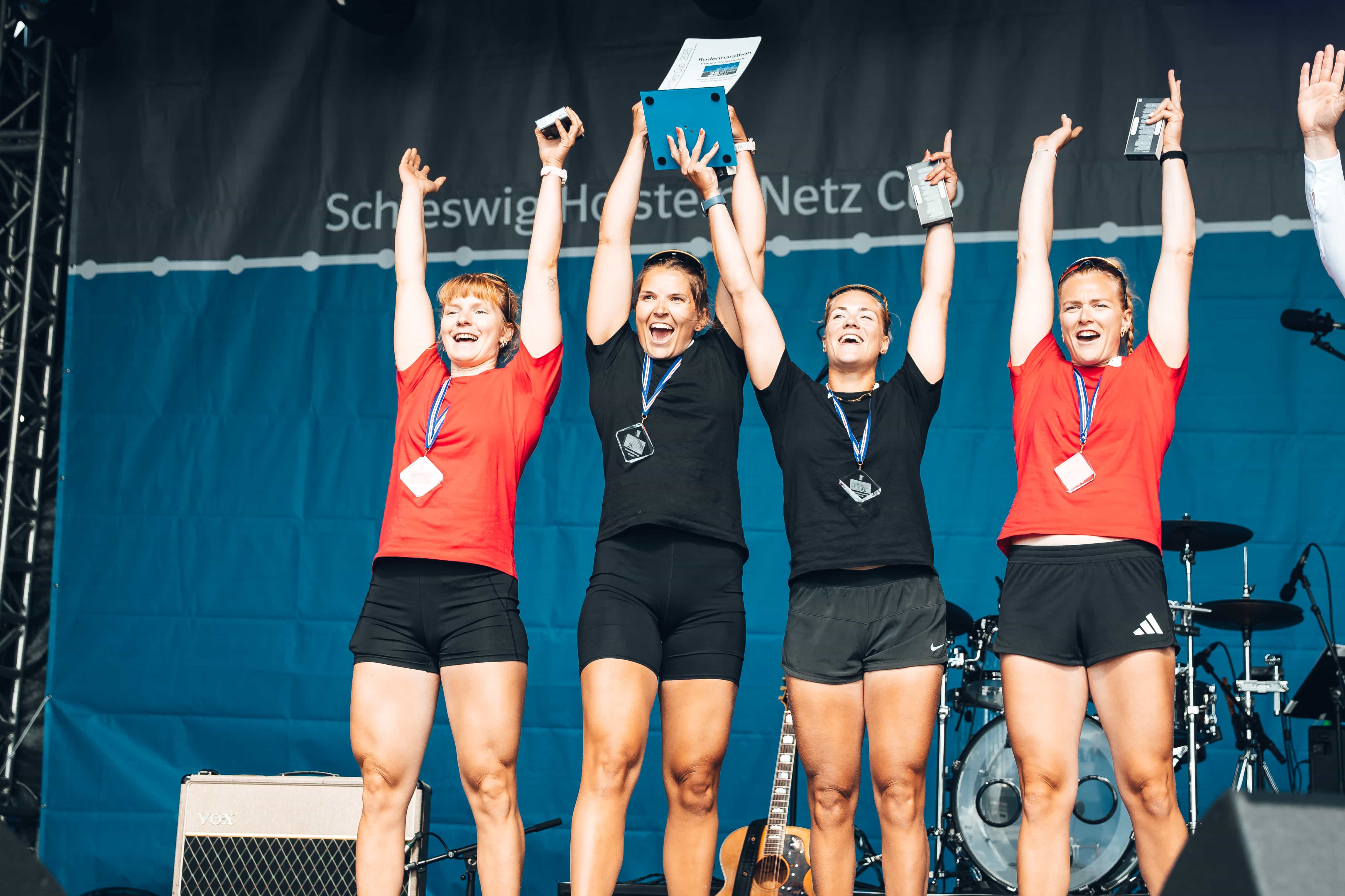 Vier Ruderinnen des deutschen Teams reißen bei der Siegerehrung die Arme hoch und freuen sich