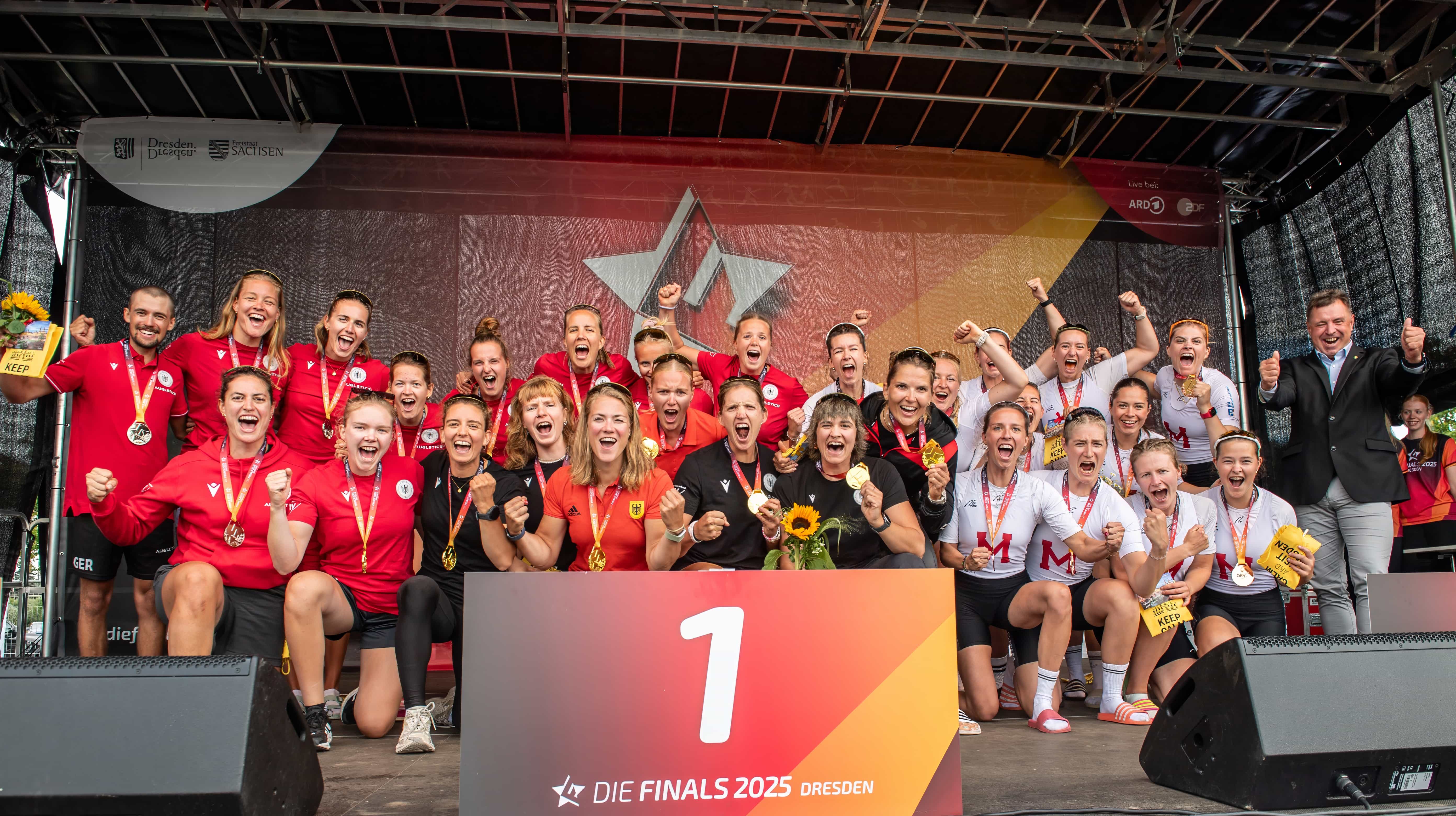 Viele Ruderinnen im Trainingsoutfit des deutschen Teams sind auf der Bühne und jubeln bei der Siegerehrung