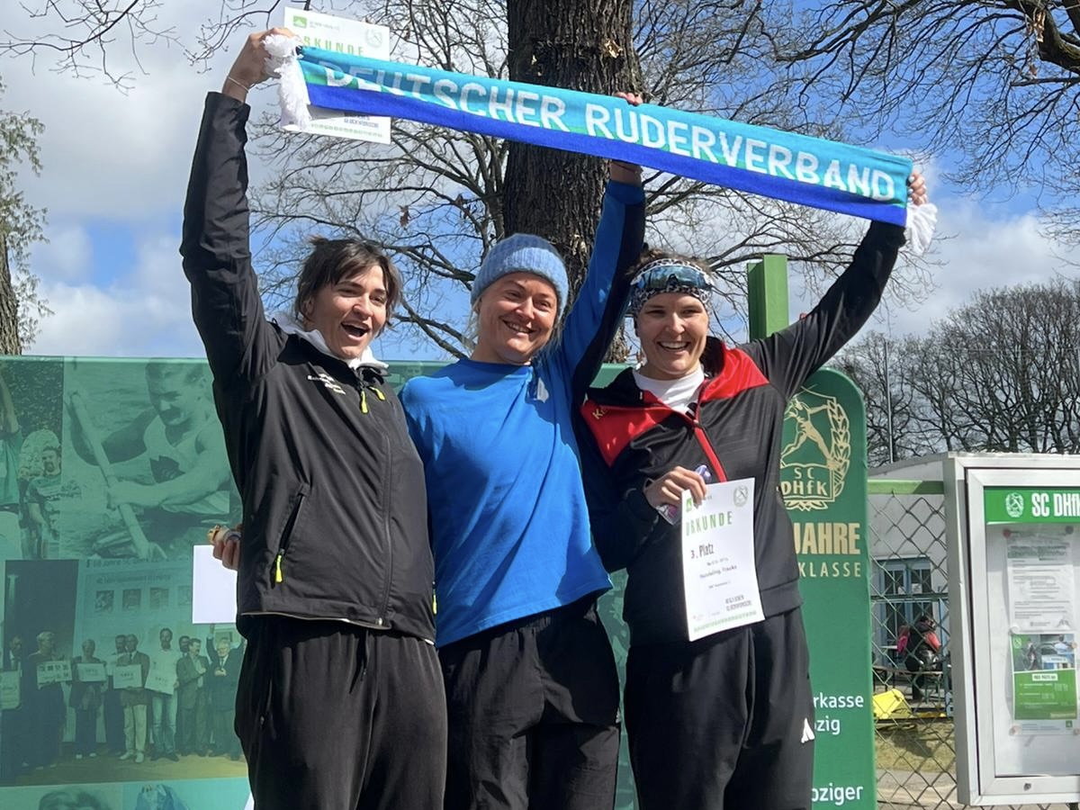 Tabea Schendekehl, Juliana Faralisch und Frauke Hundeling bei der Siegerehrung in Leipzig mit einem Schal in der Hand mit der Aufschrift Deutscher Ruderverband