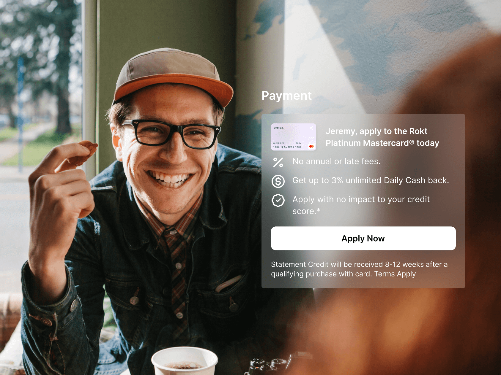 A cheerful man wearing glasses and a cap smiles while holding a bite of food and sitting near a window with coffee. A payment overlay encourages him to apply for the “Rokt Platinum Mastercard®,” offering perks like no annual fee and up to 3% cash back. The “Apply Now” button is featured prominently.