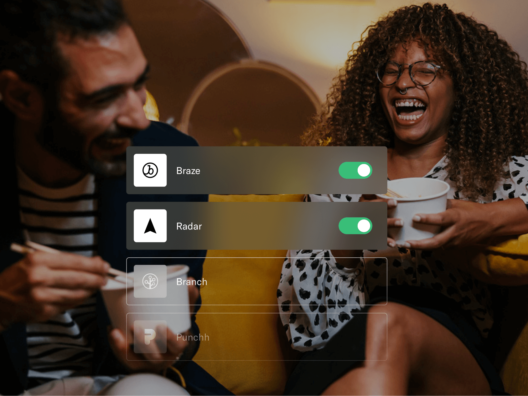 Two friends laugh while eating takeout on a couch, with an overlay showing toggled-on app integrations for Braze and Radar, and disabled options for Branch and Punchh.