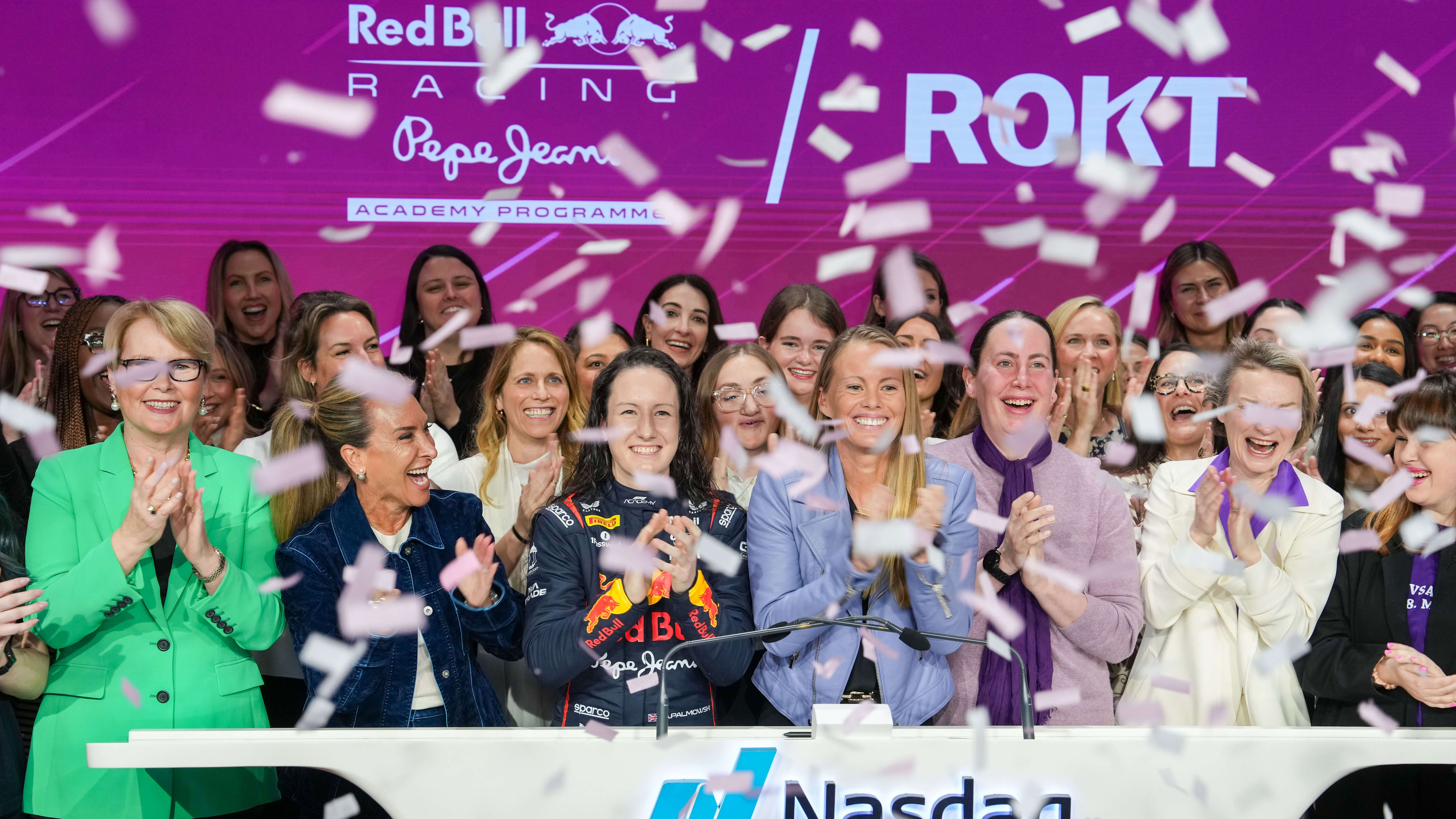 A large group of women celebrate amid falling confetti at the Nasdaq podium, with a Red Bull Racing driver in uniform at the center. The backdrop features logos for Red Bull, ROKT, and the "Pepe Jeans Academy Programme," highlighting a milestone event.