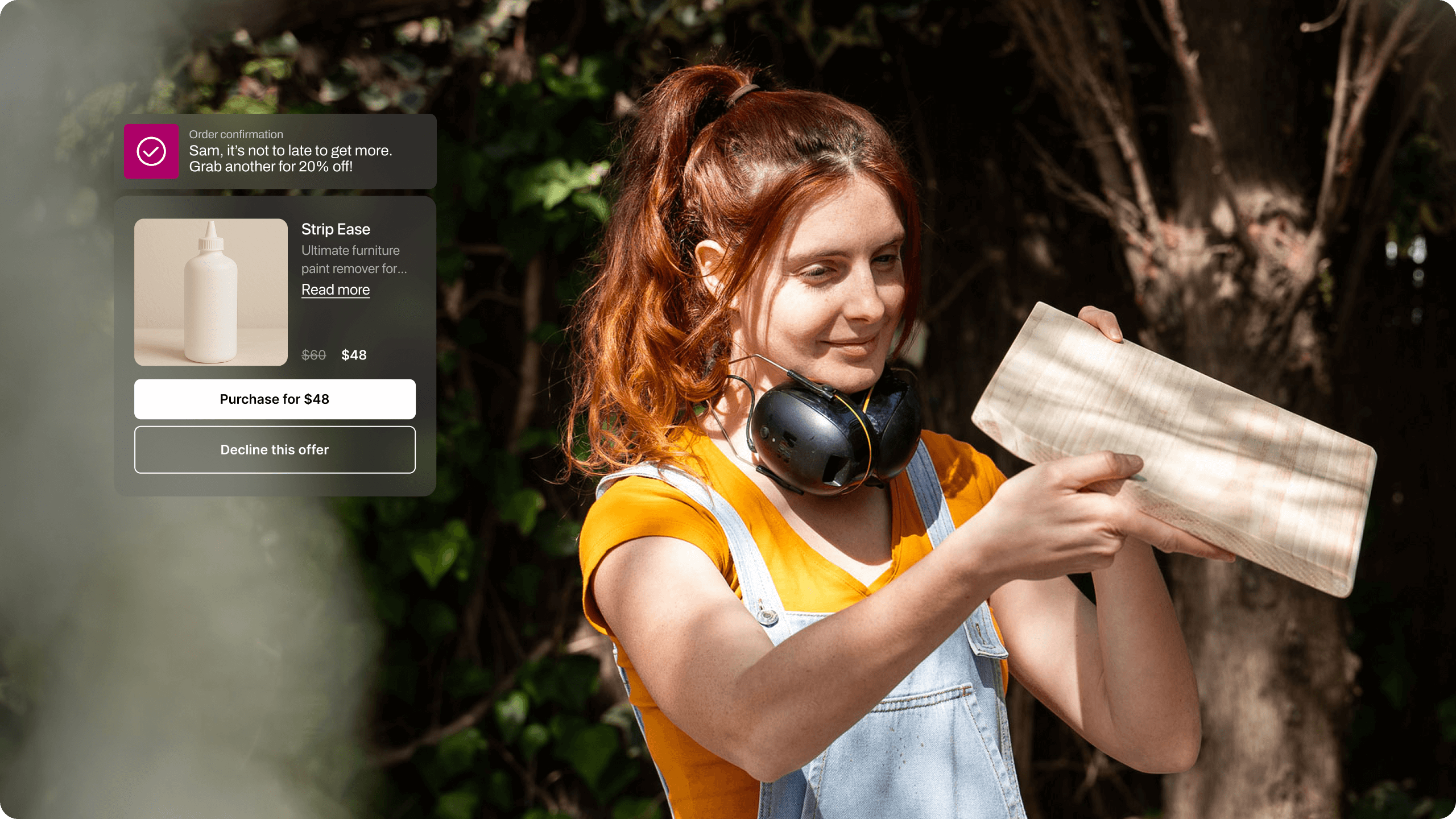 A woman with red hair tied in a ponytail stands outdoors, examining a light-colored wooden board in bright sunlight. She wears denim overalls over an orange shirt, with black protective earmuffs resting around her neck. A digital overlay on the left shows an order confirmation message and a product offer for a furniture paint remover called “Strip Ease,” discounted to $48. The image conveys a hands-on DIY moment enhanced by personalized online shopping prompts.