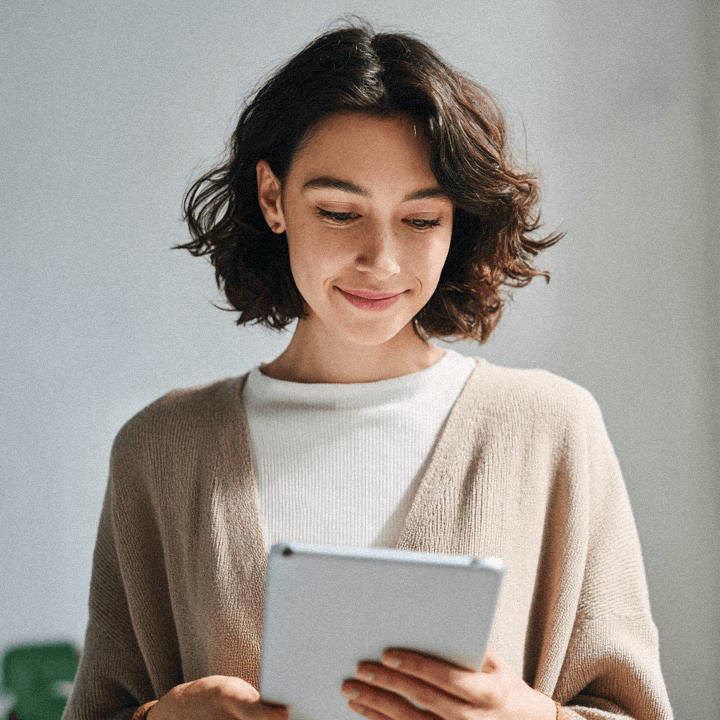 Smiling woman with short brown hair using a tablet against a plain background.