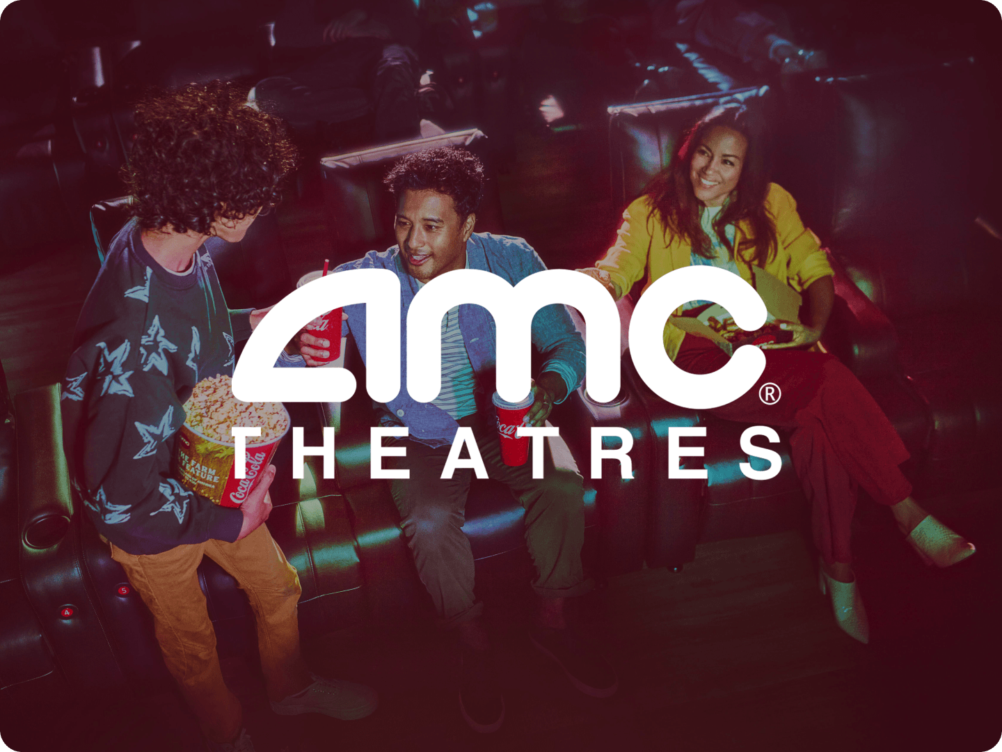 Three people sitting and standing in a movie theater with drinks and popcorn, casually chatting and smiling in reclining seats with AMC Theatres logo overlaid.
