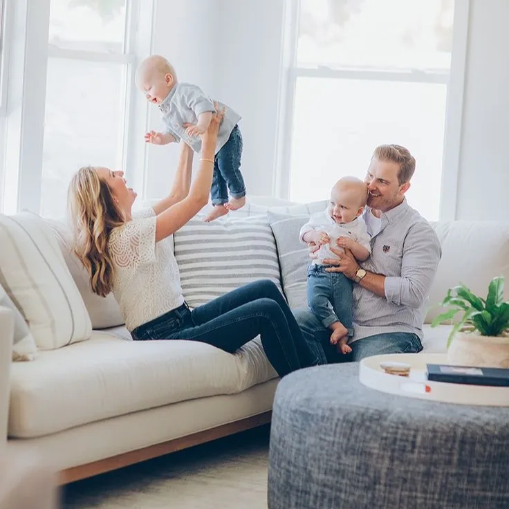 Parents playing with two babies on cozy living room couch near window