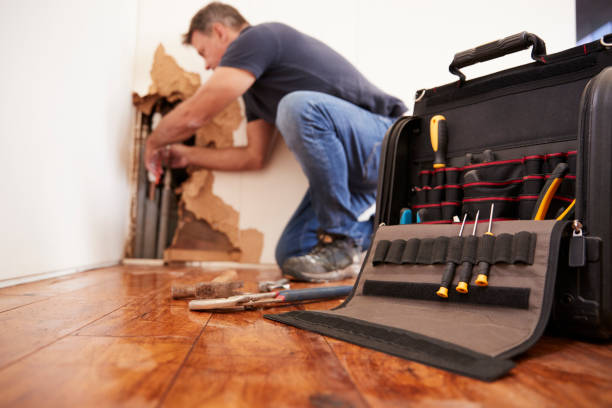 Handyman repairing wall near tool bag on wooden floor