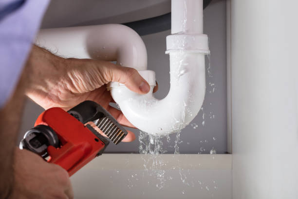 Plumber fixing a leaking pipe with a red adjustable wrench