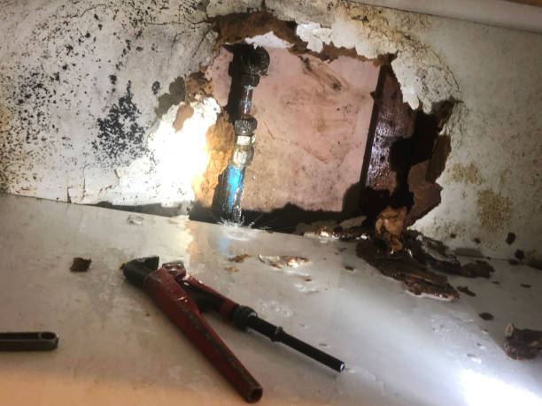 Burst pipe with water leaking through damaged wall and plumbing tools