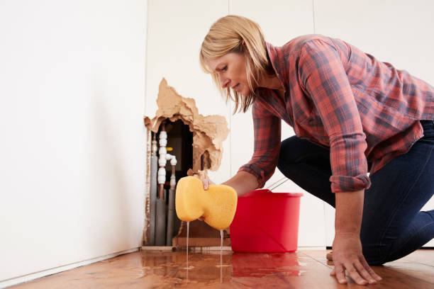 Woman cleaning water leak from burst pipe near damaged wall