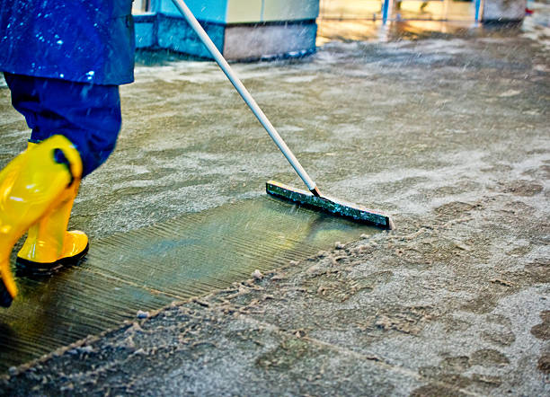 Worker in yellow boots using push broom to clean wet concrete floor