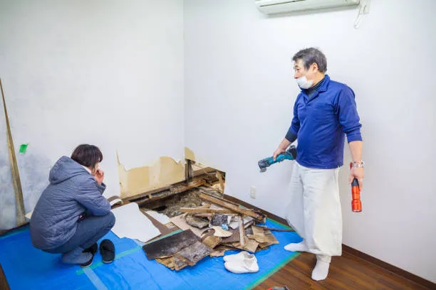 Two people working on home renovation with debris on blue tarp