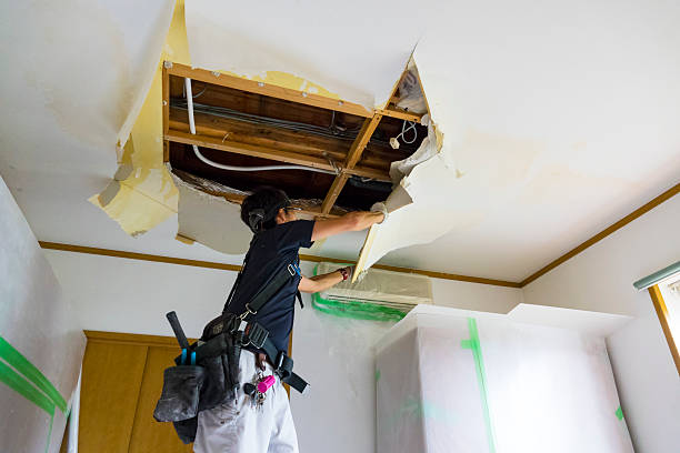 Worker repairing damaged ceiling, removing drywall with construction tools