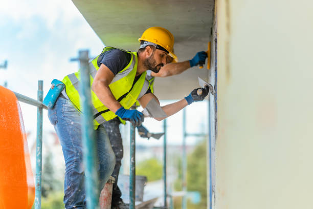 Construction worker in safety gear plastering wall on scaffolding