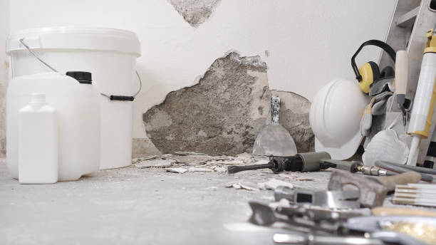 Construction tools and materials on floor with damaged concrete wall
