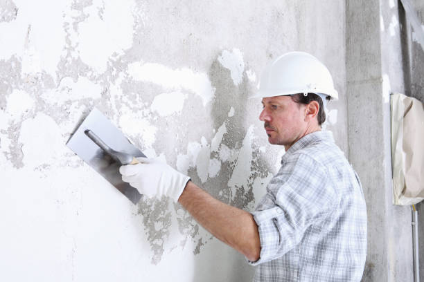 Construction worker in hard hat plastering and smoothing a concrete wall