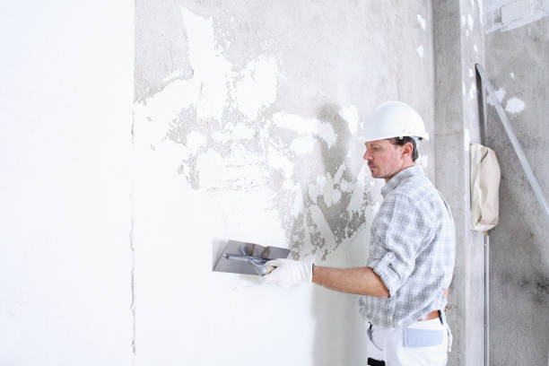 Construction worker smoothing wall with plastering tool in white hard hat