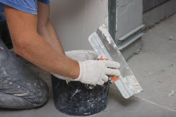Worker using putty knife and bucket to prepare wall for plastering