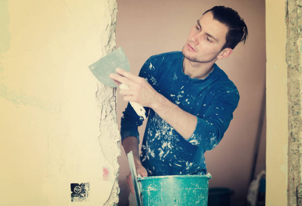 Person plastering wall with trowel and paint-splattered blue shirt