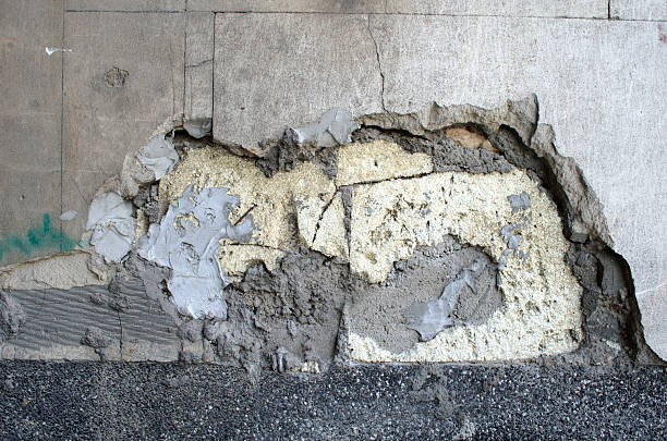Cracked and damaged concrete wall with exposed layers and broken surface