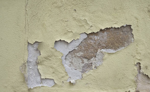 Cracked and peeling pale yellow wall with exposed concrete underneath