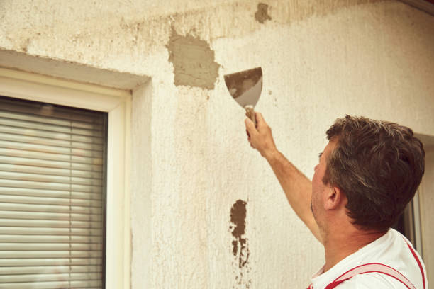 Person using putty knife to repair damaged wall near window blinds