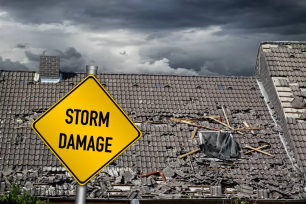 Storm damage warning sign on severely damaged roof under dark clouds