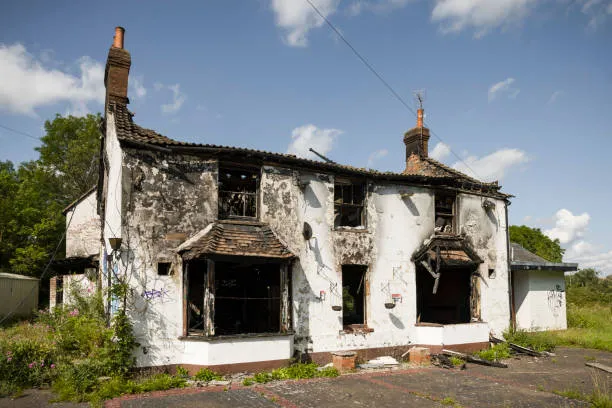 Burnt and abandoned white house with damaged windows under blue sky
