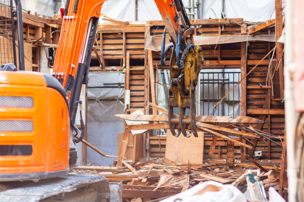 Orange excavator demolishing wooden building structure with debris around