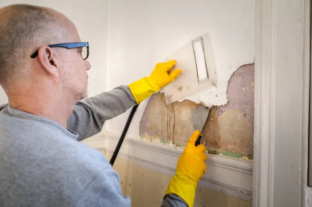 Person removing wallpaper with yellow gloves and scraper