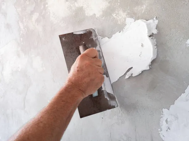 Plastering wall with putty knife, smoothing out uneven surface