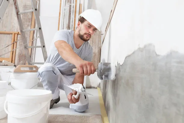 Construction worker in hard hat applying plaster or paint to wall