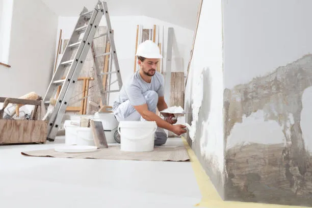 Construction worker applying plaster to wall with painting supplies nearby