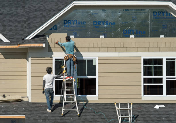 Workers installing siding on a house with ladders and construction materials